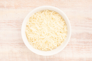 Long Basmati rice in ceramic bowl on brown wooden background. Macro. Flat lay. Vegetarian food concept