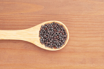 Mustard seeds in wooden spoon on yellow wooden background. Close up. Healthy diet concept