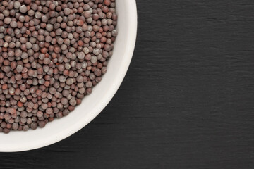Mustard seeds in white ceramic bowl on black wooden background with copy space. Close up. Vegetarian food concept