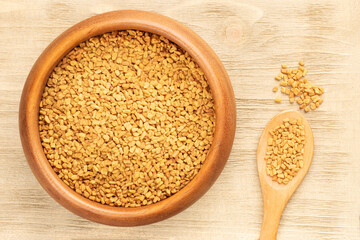 Fenugreek (Trigonella foenum-graecum) in wooden bowl and spoon on brown background. Macro. Flat lay. Diet food concept