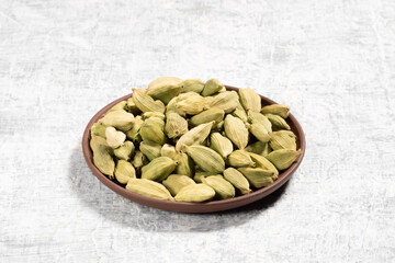 Spice green cardamom (Elettaria cardamomum) in clay plate on white concrete background. Close up. Ingredients for cooking concept