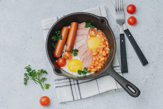 Frying pan with english breakfast. Eggs, sausages, bacon, tomatoes and beans