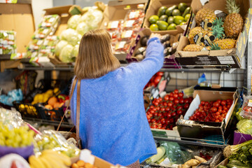 Woman choosing avocado from the counter full of products at market. View from the backside. Buying food at local market