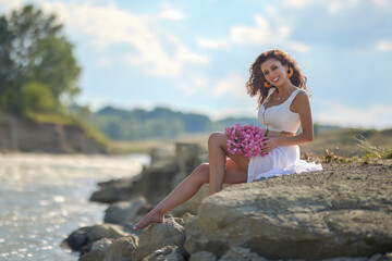 Beautiful woman in white dress on the bank of a river in summer.