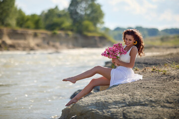 Beautiful woman in white dress on the bank of a river in summer.
