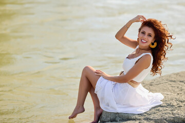 Beautiful woman in white dress on the bank of a river in summer.
