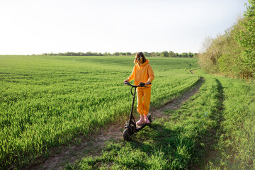 Young person in overalls riding electric scooter on green field during sunset. Concept of sustainability and eco-friendly lifestyle © rh2010