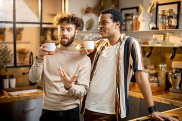 Two guys of different ethnicity having warm conversation while drinking coffee on kitchen at home. Concept of close male friendship or relationship as gay couple. Caucasian and hispanic man together