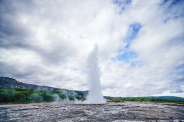 Large geyser on Iceland surrounded by lava cliffs