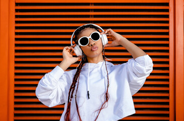 Young African American woman with braided hair wearing urban sportswear with headphones and...