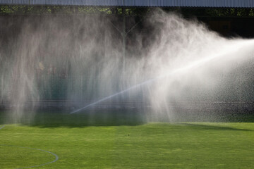Podlewanie trawy w słonecznej suszy na boisku sportowym. - obrazy, fototapety, plakaty