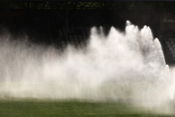 Podlewanie trawy w słonecznej suszy na boisku sportowym. - obrazy, fototapety, plakaty