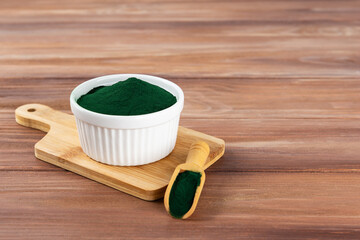 Spirulina powder in a bowl and spoon on a wooden board. Horizontal orientation, copy space.