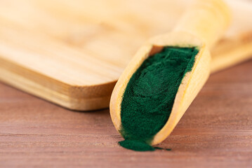 Spirulina powder in a spoon on a wooden board.