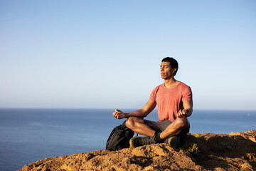 Naklejka na ściany i meble Young man meditating on top ocean cliff.