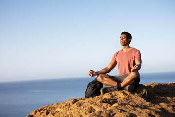 Fototapeta na wymiar Young man meditating on top ocean cliff.