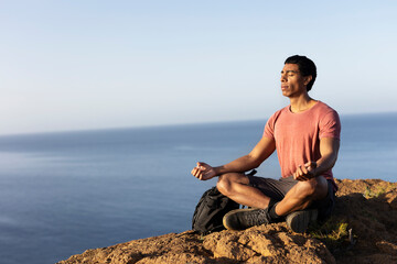 Fototapeta na wymiar Young man meditating on top ocean cliff.