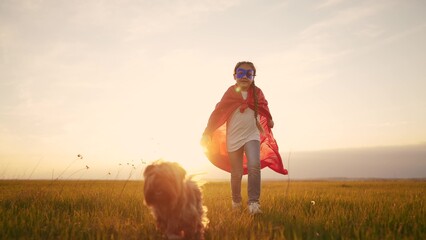girl superhero. child in a red raincoat runs with a dog outdoors in the park. happy family kid...