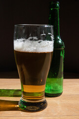 beer in a glass near a green bottle and on a black background