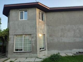 part of a two-story private gray house with plastic windows against the blue sky and greenery