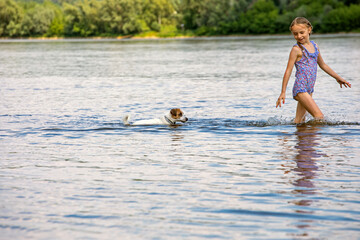 happy wet jack russell runs on water with a little girl on a sunny day. horizontal