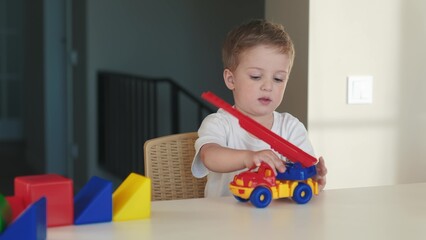 boy kid playing toy in kindergarten. happy family kid dream education concept. baby son playing with a toy fire truck on table in the kindergarten indoors. blond boy 2 years playing toys lifestyle