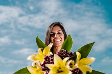 Woman smiling while holding a bouquet of yellow flowers on a sunny day with blue sky