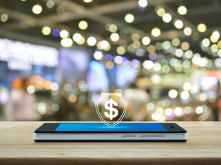 Dollar with shield flat icon on modern smart mobile phone screen on wooden table over blur light and shadow of shopping mall, Business money insurance and protection online concept