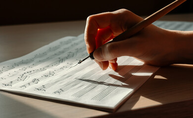 Sheet with notes and a woman's hand drawing notes with an ink pen, writing music, selective focus