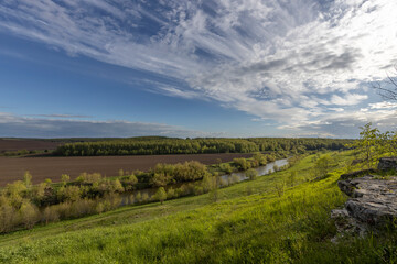 Obraz premium View of the countryside. bright greenery in the ravine. Saturated green grass against the blue sky. Plowed field on the horizon.