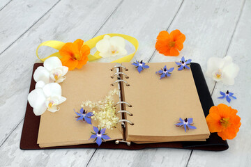 Leather bound journal or diary with blank pages for personal notes or story, with orchid flowers, nasturtium and borage herb flowers. Nature themed writing concept. On rustic wood background.