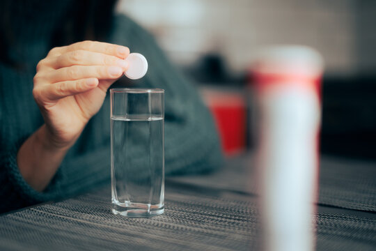 Hand Dropping A Vitamin Pill Into A Glass Of Water