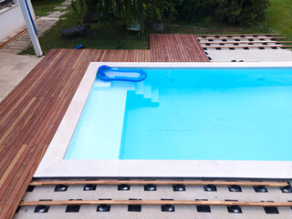 Drone flight over beautiful green garden with pool and the wooden terrace of the pool is currently in progress