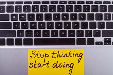 Laptop keyboard with stop thinking start doing slogan. Motivation motto on yellow paper.