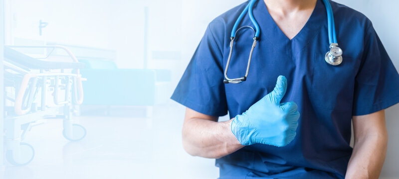 Cropped image of handsome male surgeon doctor with stethoscope in blue uniform with statoscope holding thumb up in clinic on blue hospital background. banner with copy space