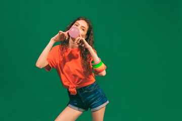 Portrait of cheerful young girl in casual summer outfit, posing with bubble gum isolated over green studio background