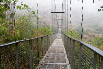Fog view on the Khndzoresk suspension bridge in the cave city in the mountain rocks. Armenia landscape attraction. Abandoned ruins in the mist. Atmospheric stock photo.