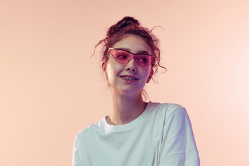 Portrait of young beautiful girl in stylish sunglasses posing isolated over pink studio background
