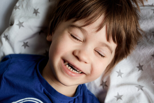 Portrait of beautiful happy 5 year child. Little boy lays on a bed and laughs from tickling. Close-up baby face. Cute caucasian appearance. Happy childhood. Home lifestyle. Brown hair and closed eyes