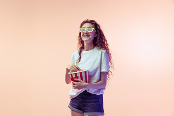 Portrait of young girl in casual outfit posing with popcorn basket isolated over pink studio background in neon light