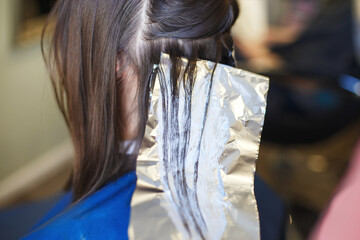 The hairdresser paints a brunette woman's hair in the beauty salon.