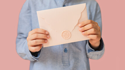Anonymous child holding pink envelope with gift certificate in his hands.Mother day concept or wedding invintation.