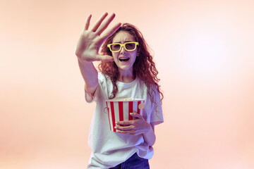 Portrait of young girl in casual outfit posing with popcorn basket isolated over pink studio background in neon light. Horror movie