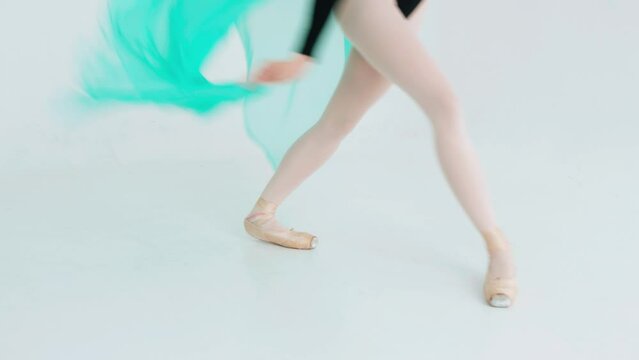 Close-up of the legs of a ballerina in pointe shoes who performs a classical dance with a turquoise veil in her hands