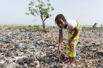 Innocent little African girl who collects recyclable waste in a landfill smiling at the camera not...