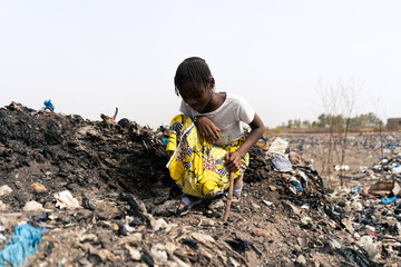 Little African girl sitting on a rubbish heap looking for recyclable materials to help her parents...