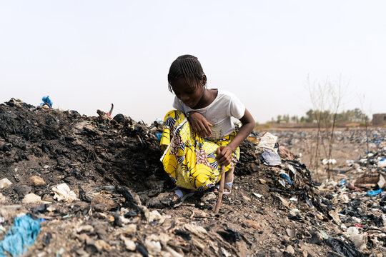 Little African Girl Sitting On A Rubbish Heap Looking For Recyclable Materials To Help Her Parents In Need