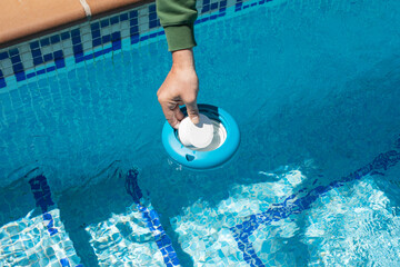 Operator inserting a chlorine tablet into a floating pool dispenser to level the ph.Chlorine and...