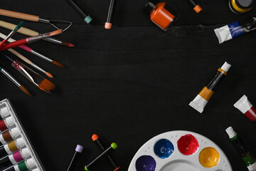 Flat lay watercolors, palette and paint brushes on black wooden table. Artist or designer workplace