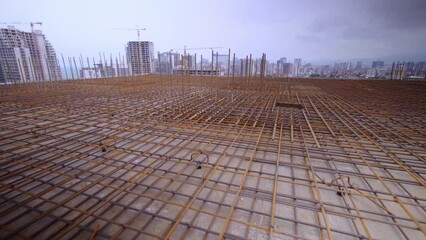 Iron reinforcement is basis for pouring foundation of house with concrete slab. Construction design, engineering communications. Top floor or roof of building under construction with view of city.
